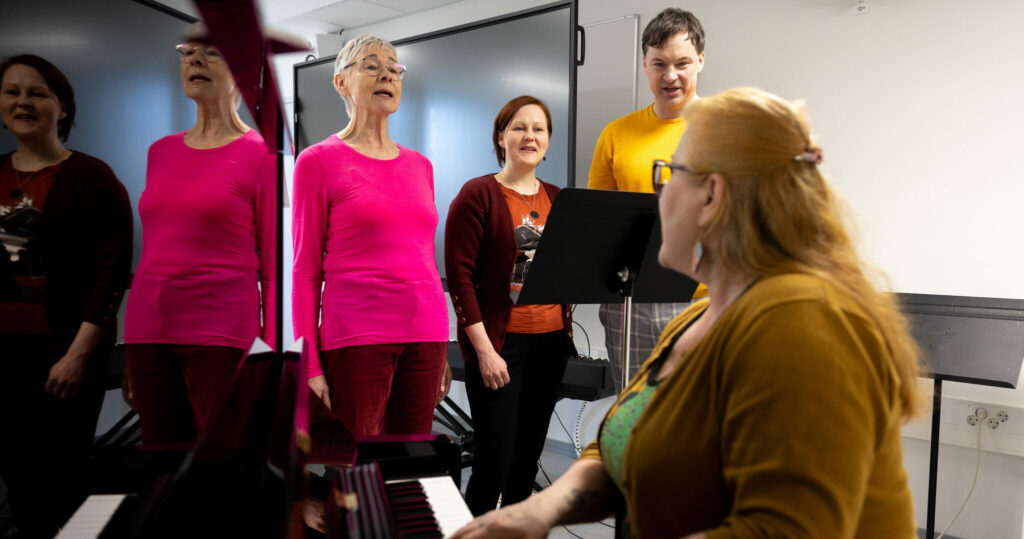 Ryhmä ihmisiä laulamassa pianon säestyksellä